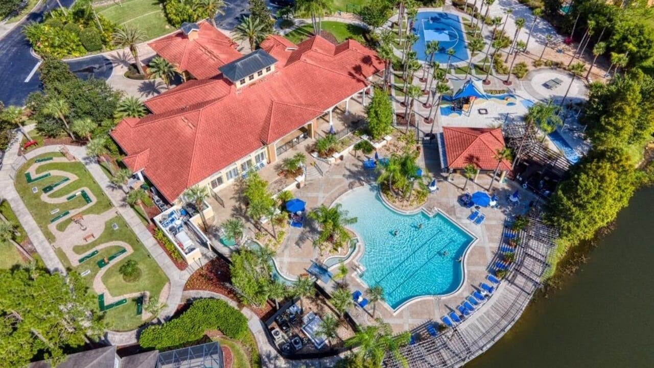 Aerial of Terra Verde Resort: red-roofed clubhouse, freeform pool, mini golf, playground, and the lake