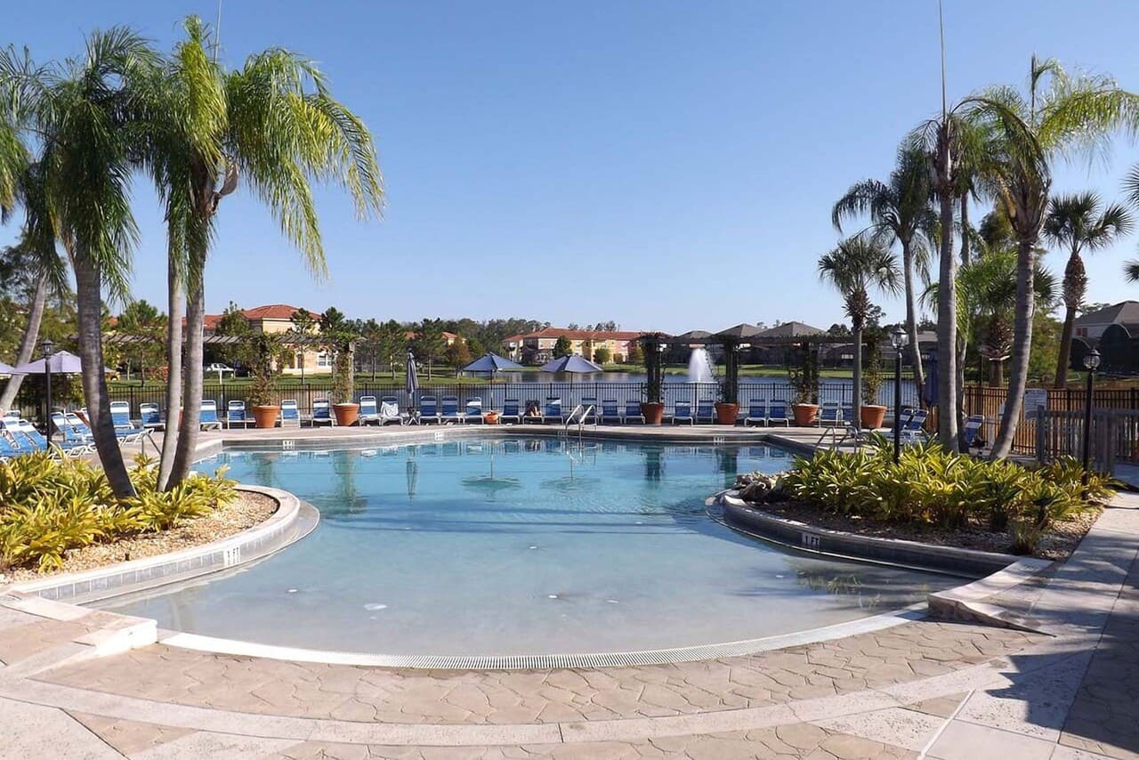Beach-entry pool at Terra Verde, lounge chairs along the far side, lake fountain beyond